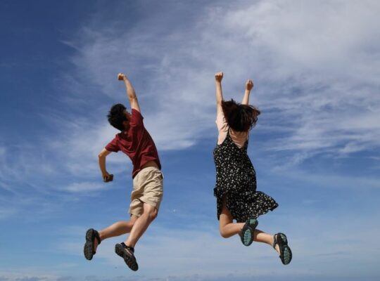 Man and woman leaping in the air with blue skies on a clear and sunny day